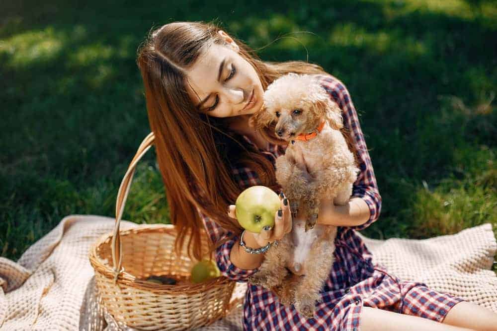 A cute lady carrying her pet dog in her arm and holding an apple.